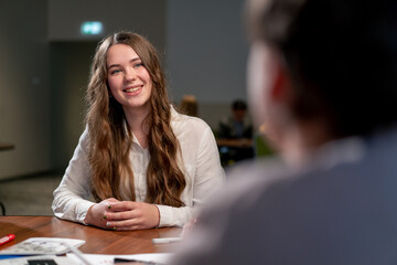 a young smiling girl talks about herself at an interview with a potential hiring manager in a large...
