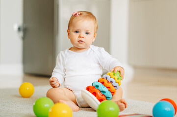 Obraz premium Cute baby girl is sitting on the floor at home while playing with her toys.