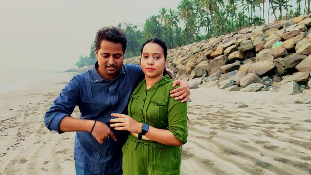 Drunk man stagger or falter female handle him on a beach with rocks in the background