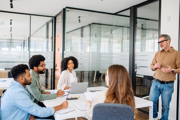In a modern office, a man in a tan shirt gestures during a dynamic presentation to attentive...