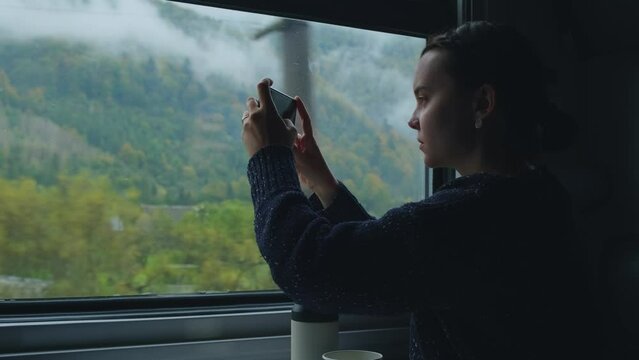 Woman taking pictures of Carpathian mountains from train. Fog over mountain peaks and green forest, Female passenger or traveler takes photo of mountain landscape outside the window while sitting