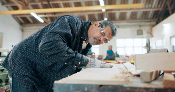 Senior man, carpenter and blowing wood in workshop for dust, shavings or smooth finish at manufacture. Mature male, builder or craftsman working on bench, table or work desk at warehouse or shop