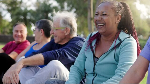 Multiracial group of senior people having fun after exercise yoga workout at park. African woman laughing with friends