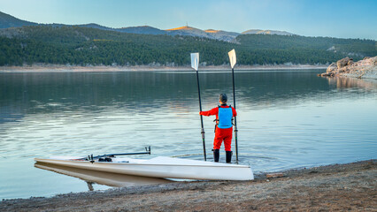 Senior male rower and a coastal rowing shell is landing on a rocky shore of Carter Lake in fall or...