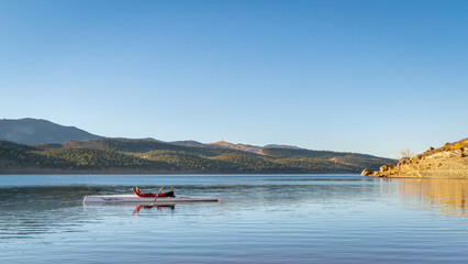 male rower is resting in his rowing shell on Carter Lake in fall or winter scenery in northern...