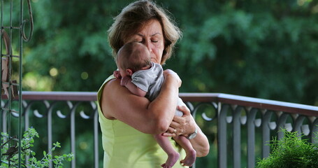 Grand-mother holding newborn baby grand-son in outside balcony
