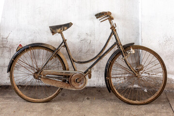 Dusty, rusty old woman's bicycle leaning against off-white wall