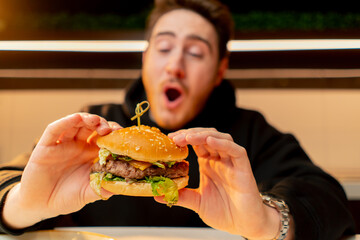 close-up man with enjoy biting delicious juicy cheeseburger in cafe restaurant junk food calories