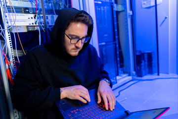 concentrated hooded hacker in data center hacking software system vulnerable cyber security server...