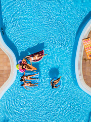 Aerial vertical view of group of women friends have fun together in summer holiday vacation at pool resort with coloured inflatables lilos on the blue water - obrazy, fototapety, plakaty