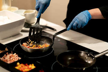 close-up of a chef in an open kitchen in a hotel preparing an omelette with vegetables during...