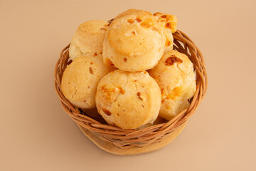 Brazilian cheese bread inside a wooden basket in a beige clean background in front top view