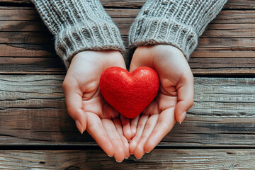 A pair of hands holds a small red heart set against the backdrop of a rustic wooden surface