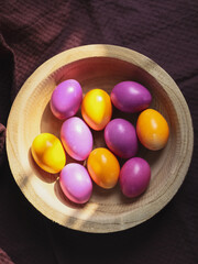 Obraz na płótnie Canvas Colorful Easter eggs in a wooden plate on a dark burgundy kitchen towel.