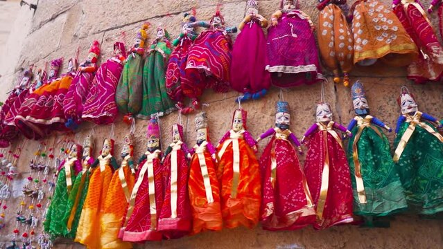 Colorful puppets hanging on wall of market in Jaisalmer fort, Rajasthan, India. Puppets dressed in beautiful traditional clothes selling in street market of India. Culture and traditions of India.
