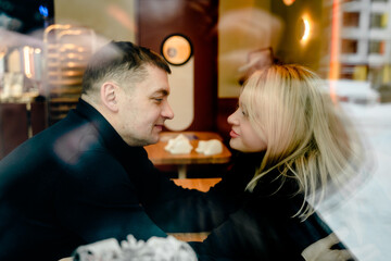 Love romantic couple lovestory. Man hugging woman, kissing blonde girl in cozy coffee shop cafe. Romantic family date. Sitting at window table in restaurant. Intimate romance atmosphere