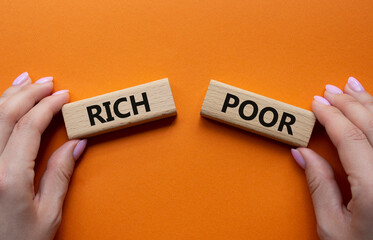 Rich vs Poor symbol. Concept word Rich vs Poor on wooden blocks. Businessman hand. Beautiful orange background. Business and Rich vs Poor concept. Copy space