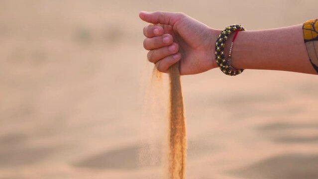 Close up shot of hand pouring desert sand at Khuri sand dunes in Thar desert at Rajasthan, India. Indian Female hand playing with sand, releasing dropping sand. Travel and holidays concept.