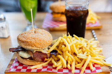 Two double cheeseburgers with bacon and fries on bar with drinks