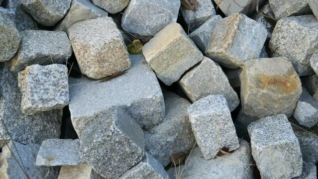 Gray cobble stones for paving roads in a pile. Piled worked granite stones of square shape.