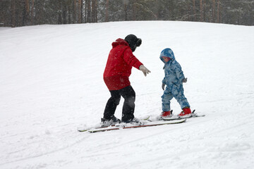 Fototapeta na wymiar A ski instructor teaches a child to ski on a snowy slope. A frosted pine forest in the background. Copy space.