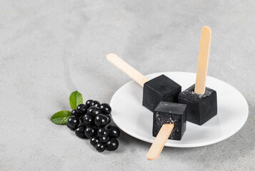 Vegan Black Matcha Ice Cream in the shape of a mini cube on a wooden stick. On a plate. Light background. Close up