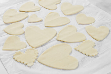 Fototapeta na wymiar Cut out hearts of various shapes and sizes from raw dough on white parchment.