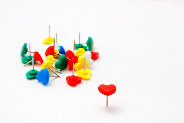 Red heart shaped thumbtack standing in front of other fallen ones of a different color