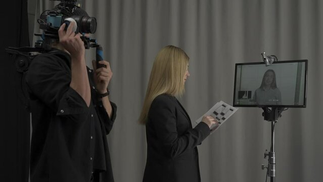 Side view of a woman director and cameraman in the studio in front of the monitor. Female director with script nods her head approvingly, and gives instructions to the presenter behind the scenes.