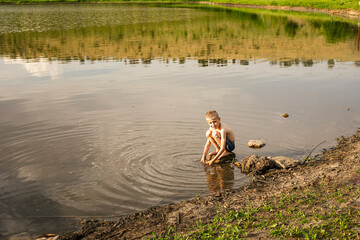 Full length image of a preschool boy playing in water, they play by the lake, old boat background. Horizontal view. Copy space.