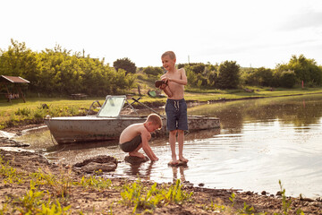 Two brothers are sitting in the water by the lake, trying to look for stones, shells, having a nice...
