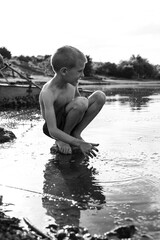 Profile image of a preschool boy playing in water, they play by the lake, old boat background.Black and white image.