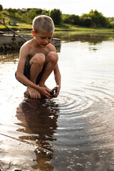 Full length image of a preschool boy playing in water, they play by the lake, old boat background. Vertical view.