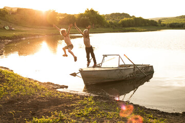 Full length image of a two little blondes boys is having fun jumping from the boat on the shore of...