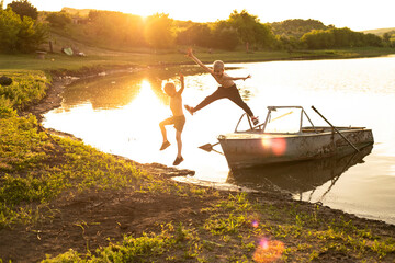 Full length image of a two little boys, playing and  having fun jumping from the boat on the shore...