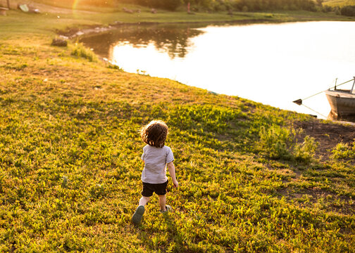Back view of a little boy running towards the lake, beautiful sunset in the background.