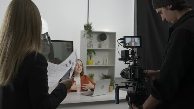 The crew backstage. Female producer, cameraman with camera n the studio during filming. A female producer with storyboard sheets looks at the monitor with the host, gives instructions to the operator.