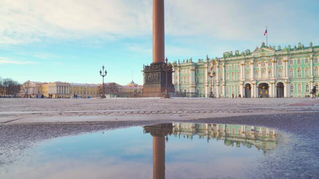 Saint-Petersburg, Russia - Feb 02 2024, a panoramic view of Palace square with mirror puddle, close-up of human legs jumping past, with the Winter palace on background, Saint Petersburg, Russia 