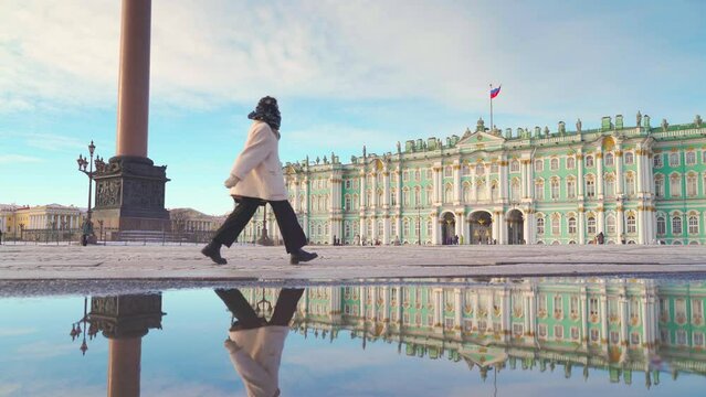 Saint-Petersburg, Russia - Feb 02 2024, 4k, a panoramic view of Palace square with mirror puddle and girl the girl walking quickly by, with Winter palace on background, Saint Petersburg, Russia