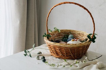 Happy Easter! Stylish easter basket with natural dyed eggs, meat, bread, butter, beets and spring flowers on rustic table. Traditional easter orthodox holiday food and cherry bloom