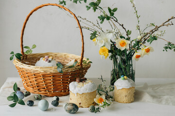 Fototapeta na wymiar Stylish Easter bread, eggs and basket with food with spring flowers on rustic table. Happy Easter! Traditional easter holiday food. Modern natural dye eggs and daffodils and cherry blossom