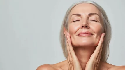 Rollo Schönheitssalon Gorgeous senior older woman with closed eyes touching her perfect skin. Beautiful portrait mid 50s aged woman advertising facial antiage lift products salon care tighten skin isolated on white.