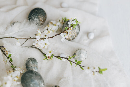 Happy Easter! Stylish easter eggs and spring flowers on linen rustic table. Natural painted marble eggs and cherry blooms. Modern minimal still life