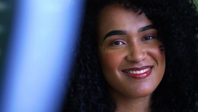 One young Brazilian woman portrait looking at camera smiling, tight close-up face of a joyful person with curly hair of African descent in 20s