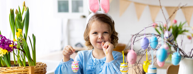 Portrait of cute pretty smiling little girl in blue dress and bunny rabbit ears preparing easter...