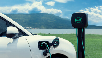 Electric car plug in with charging station, recharge battery by EV charger cable display smart digital battery status hologram with nature background. Futuristic green energy infrastructure.Peruse