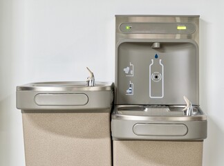 Water bottle refilling station with twin drinking fountains isolated by a plain white wall. Touchless automated eco friendly technology.