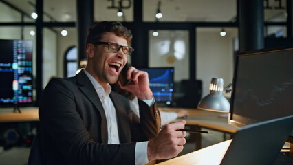 Cheerful manager enjoying call news in evening workplace. Stock happy man broker