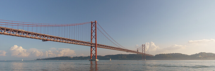 Panorama of red bridge 25 de Abril Bridge and statue of Cristo Rei during a slightly misty day,...