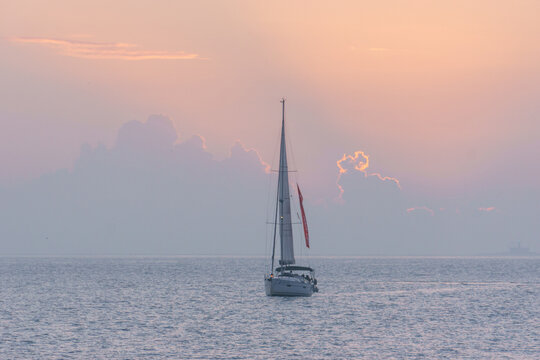 Sea with sailing boat in the sun set in front of a cloudy sky